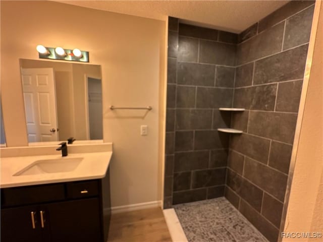 bathroom featuring vanity, hardwood / wood-style floors, a textured ceiling, and a tile shower