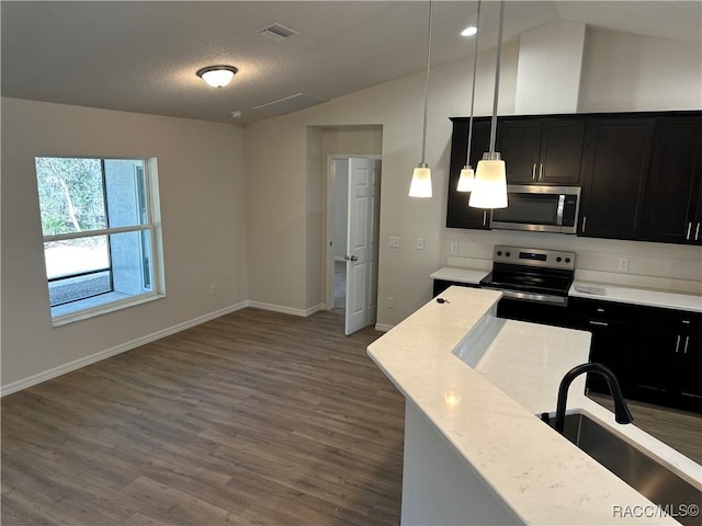 kitchen with pendant lighting, sink, appliances with stainless steel finishes, light stone countertops, and vaulted ceiling