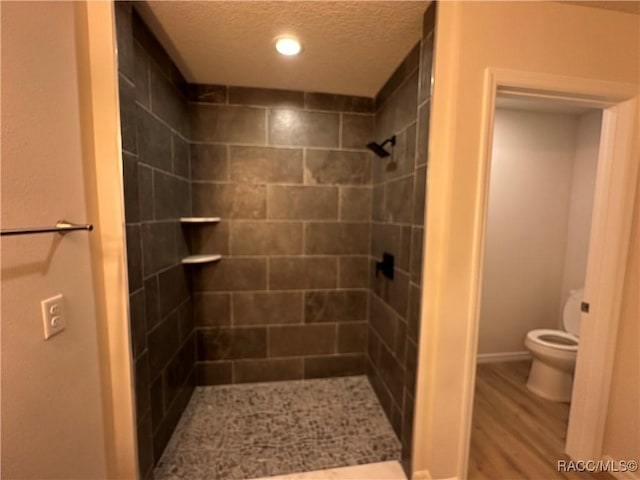 bathroom featuring tiled shower, wood-type flooring, toilet, and a textured ceiling