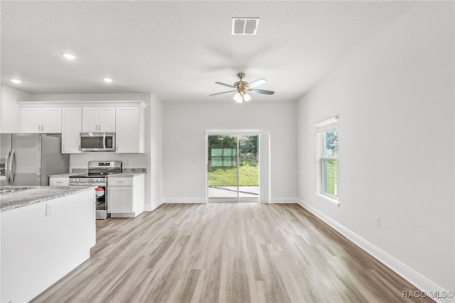 kitchen with a textured ceiling, light wood-type flooring, stainless steel appliances, and white cabinetry