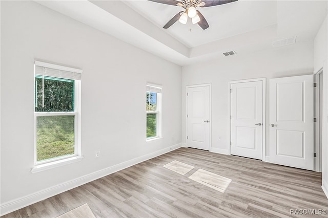 unfurnished bedroom featuring light hardwood / wood-style floors, a raised ceiling, and ceiling fan