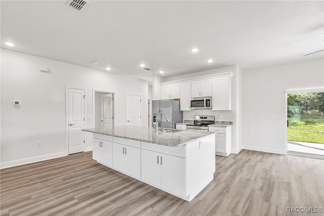 kitchen featuring a center island with sink, white cabinets, sink, light wood-type flooring, and appliances with stainless steel finishes