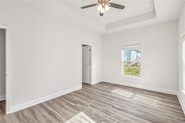 unfurnished room featuring ceiling fan, a raised ceiling, and light hardwood / wood-style flooring