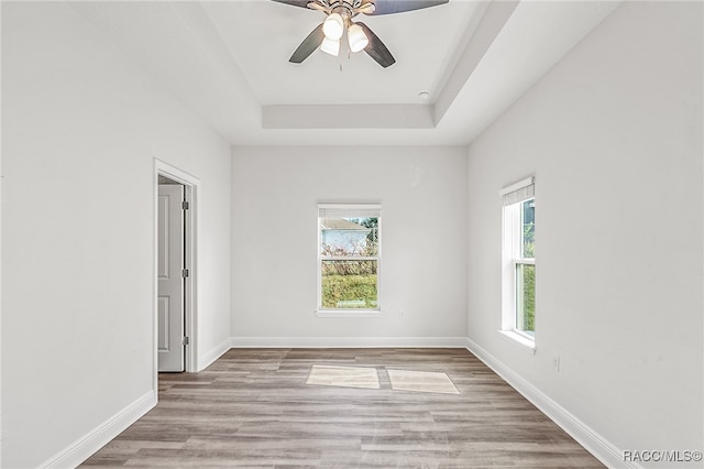 spare room featuring a tray ceiling, ceiling fan, plenty of natural light, and light hardwood / wood-style floors