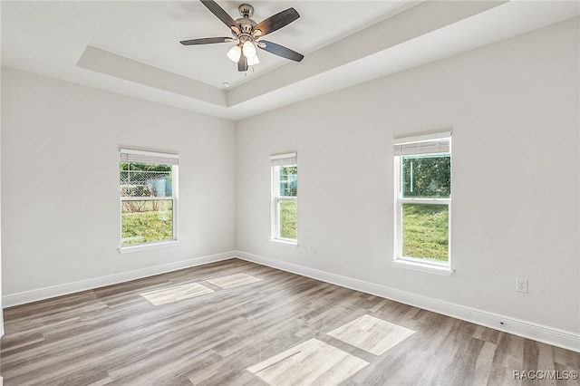 spare room with ceiling fan, light hardwood / wood-style floors, and a raised ceiling