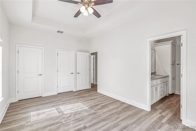 44 W Lynnhaven Pl, Citrus Springs, FL 34434 - unfurnished bedroom featuring light wood-type flooring, baseboards, a sink, a raised ceiling, and ensuite bath