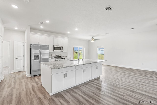 kitchen featuring white cabinets, light wood-type flooring, stainless steel appliances, and an island with sink