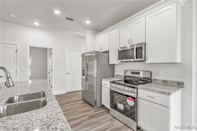 kitchen with appliances with stainless steel finishes, light wood-type flooring, light stone counters, sink, and white cabinets