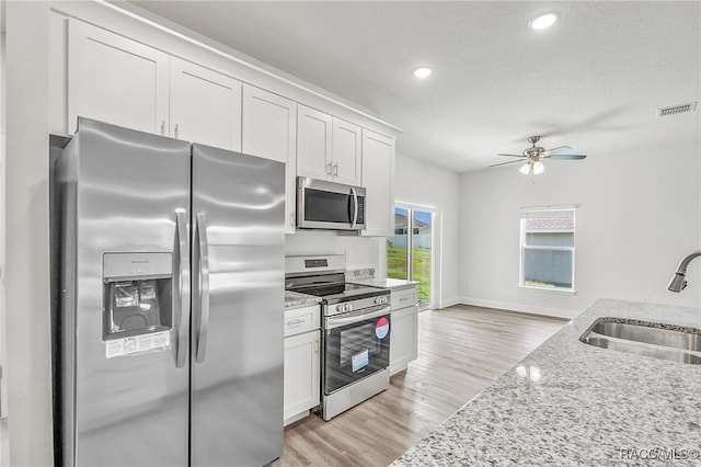 kitchen with light stone countertops, light wood-type flooring, stainless steel appliances, sink, and white cabinetry