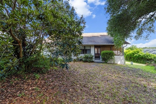 view of property hidden behind natural elements with a shingled roof