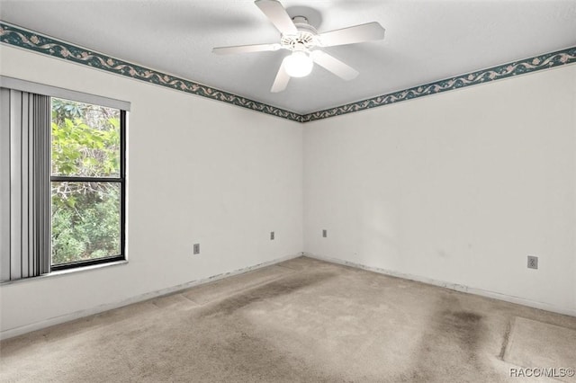 carpeted spare room featuring baseboards and a ceiling fan