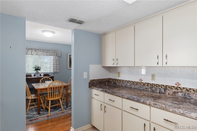 kitchen with decorative backsplash, a textured ceiling, light wood-type flooring, and dark stone countertops