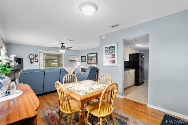 dining area with ceiling fan, light wood-type flooring, and a textured ceiling