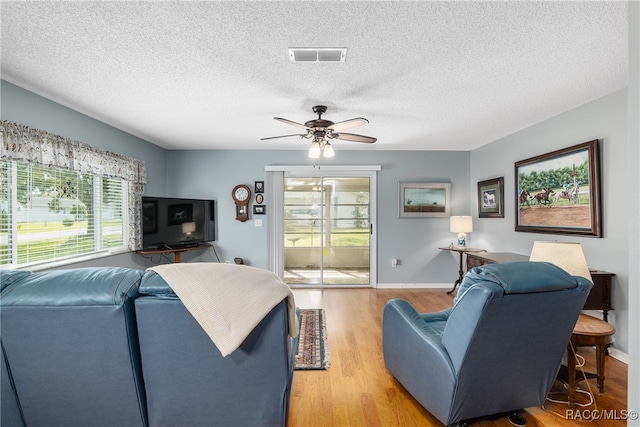 living room featuring ceiling fan, a textured ceiling, and light wood-type flooring