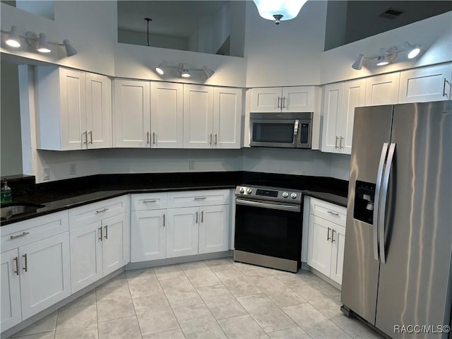 kitchen with light tile patterned floors, a towering ceiling, stainless steel appliances, white cabinets, and dark stone counters