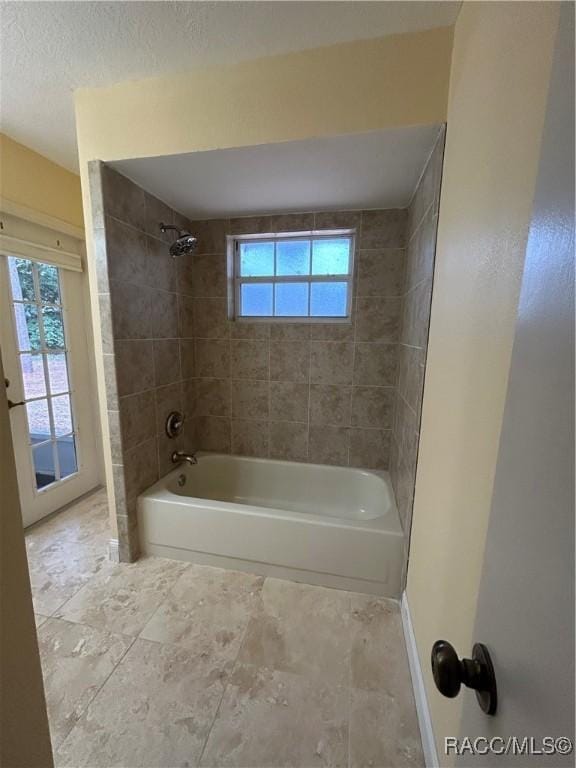 bathroom featuring a textured ceiling, plenty of natural light, and tiled shower / bath