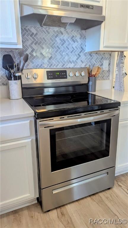 kitchen with backsplash, stainless steel electric range oven, light hardwood / wood-style flooring, and white cabinets