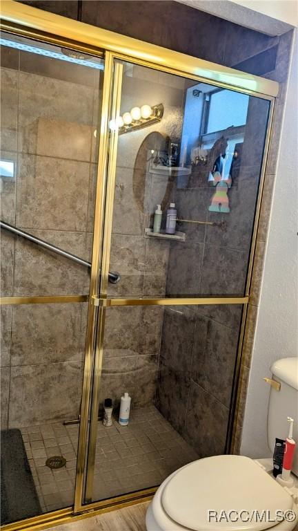 bathroom with hardwood / wood-style floors, a shower with door, and toilet