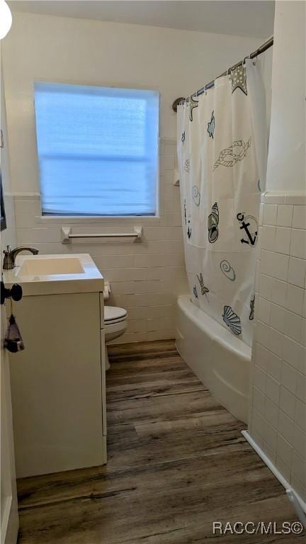 full bathroom featuring tile walls, hardwood / wood-style flooring, vanity, toilet, and shower / bathtub combination with curtain