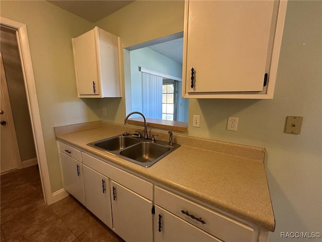 kitchen featuring dark tile patterned floors, sink, and white cabinets