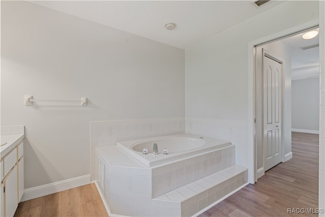 bathroom featuring hardwood / wood-style floors, vanity, and a relaxing tiled tub