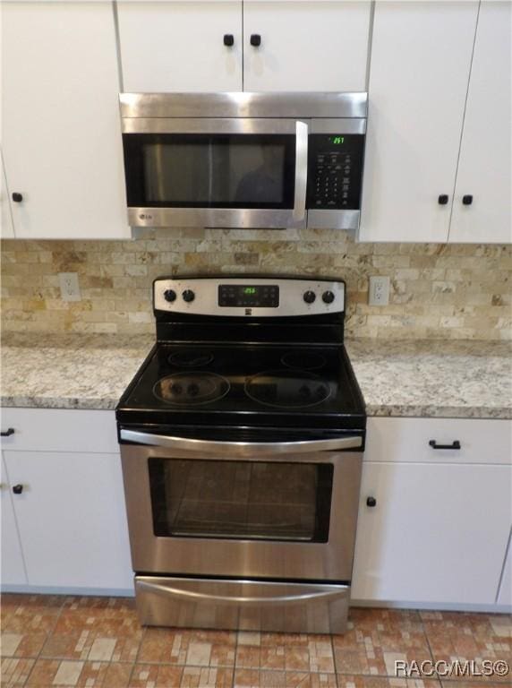 kitchen with white cabinetry, stainless steel appliances, light stone countertops, and decorative backsplash