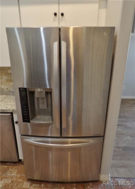 details featuring stainless steel refrigerator with ice dispenser, white cabinetry, light stone countertops, and backsplash