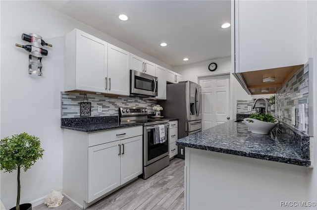 kitchen with backsplash, white cabinets, light hardwood / wood-style flooring, dark stone countertops, and stainless steel appliances