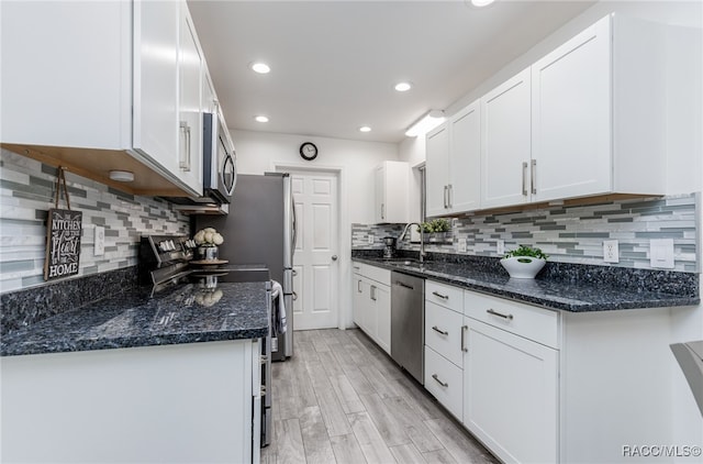 kitchen with backsplash, white cabinetry, stainless steel appliances, and light hardwood / wood-style flooring