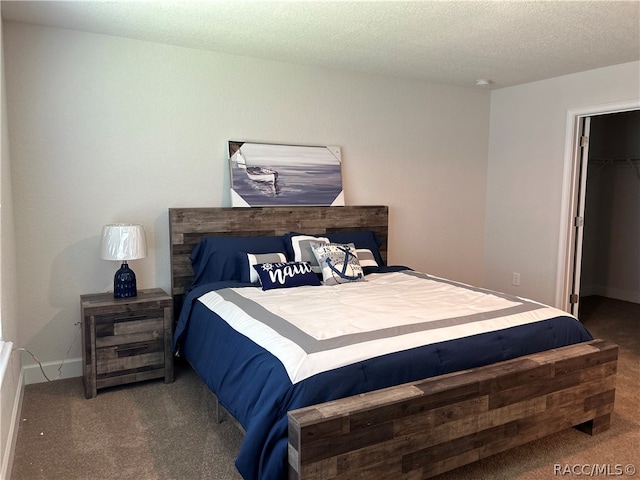 bedroom featuring a spacious closet, a closet, a textured ceiling, and dark colored carpet