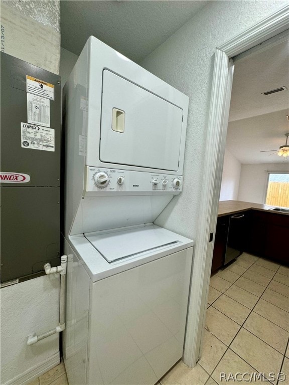 laundry area with ceiling fan, light tile patterned floors, stacked washing maching and dryer, and a textured ceiling