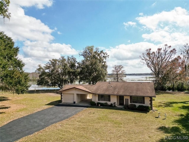 single story home featuring a carport, a water view, driveway, and a front lawn