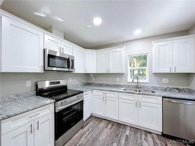 kitchen featuring stainless steel appliances, white cabinets, light stone counters, and sink