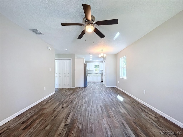 unfurnished living room featuring ceiling fan with notable chandelier, a textured ceiling, and dark hardwood / wood-style flooring