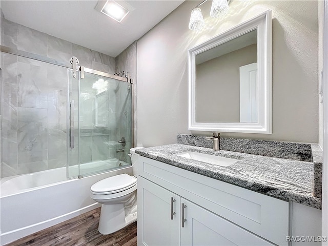 full bathroom featuring wood-type flooring, combined bath / shower with glass door, vanity, and toilet