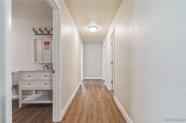 hall featuring baseboards, light wood-type flooring, and a textured ceiling