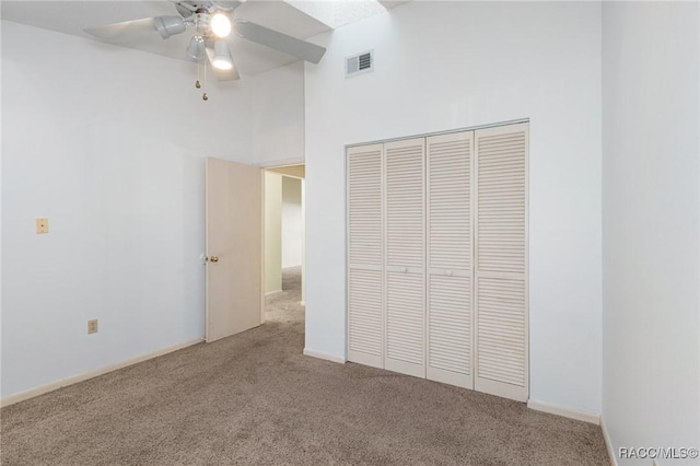 unfurnished bedroom featuring carpet flooring, a towering ceiling, a closet, and ceiling fan