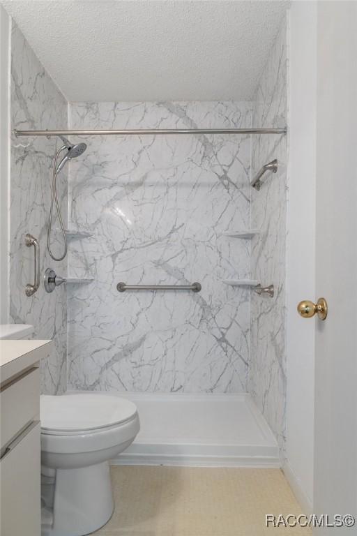 bathroom featuring tiled shower, vanity, a textured ceiling, and toilet