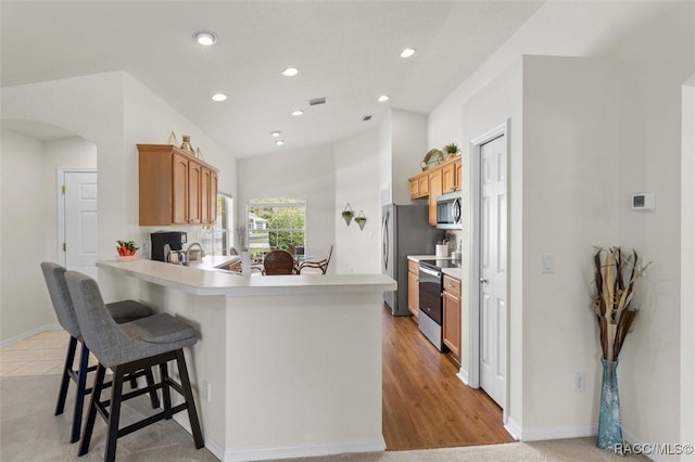 kitchen with arched walkways, appliances with stainless steel finishes, a breakfast bar area, a peninsula, and light countertops