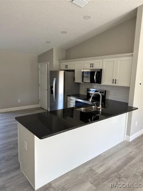 kitchen featuring stainless steel appliances, dark countertops, lofted ceiling, light wood-style flooring, and white cabinets