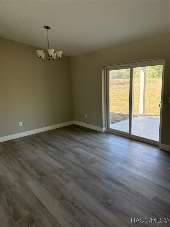 empty room with dark wood-type flooring, a notable chandelier, and baseboards