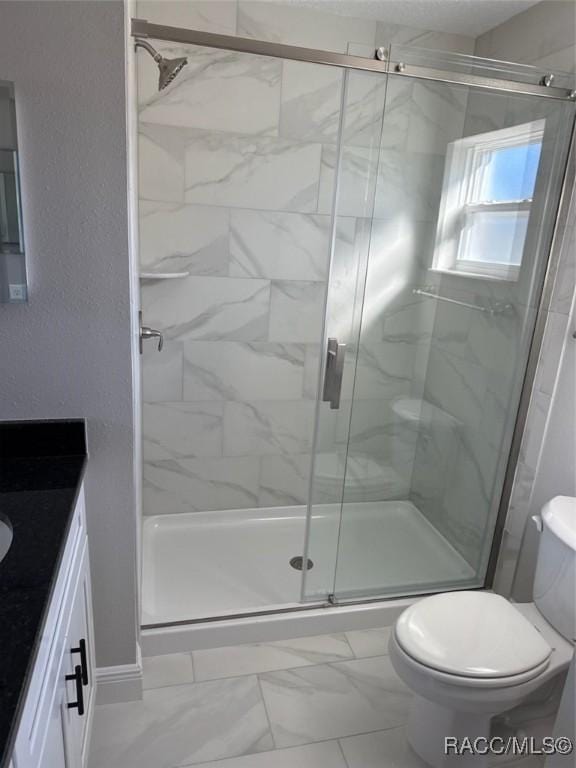 bathroom featuring marble finish floor, a textured wall, toilet, a stall shower, and vanity