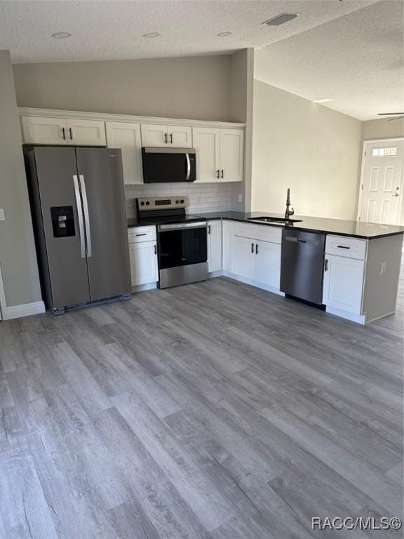 kitchen with dark countertops, visible vents, appliances with stainless steel finishes, a sink, and a peninsula