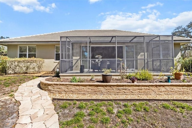 rear view of house with a tile roof, glass enclosure, and stucco siding