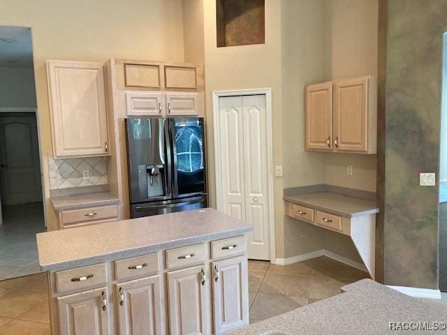 kitchen with backsplash, a towering ceiling, refrigerator with ice dispenser, light tile patterned floors, and a kitchen island