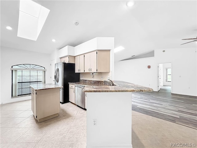 kitchen with light stone counters, vaulted ceiling with skylight, a kitchen island, and appliances with stainless steel finishes