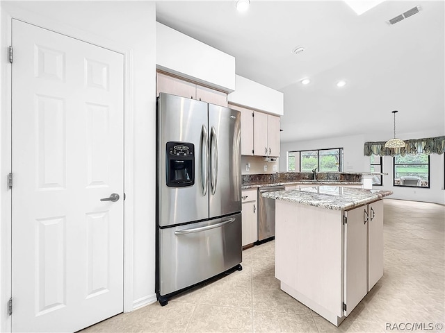 kitchen featuring light stone countertops, decorative light fixtures, a kitchen island, white cabinetry, and stainless steel appliances