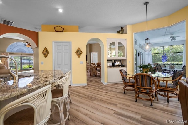 dining space featuring arched walkways, a ceiling fan, visible vents, and light wood-type flooring