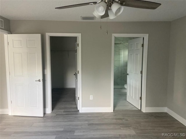 unfurnished bedroom with connected bathroom, a spacious closet, light wood-type flooring, a closet, and ceiling fan