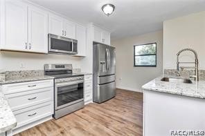 kitchen with light stone countertops, white cabinetry, sink, stainless steel appliances, and light wood-type flooring